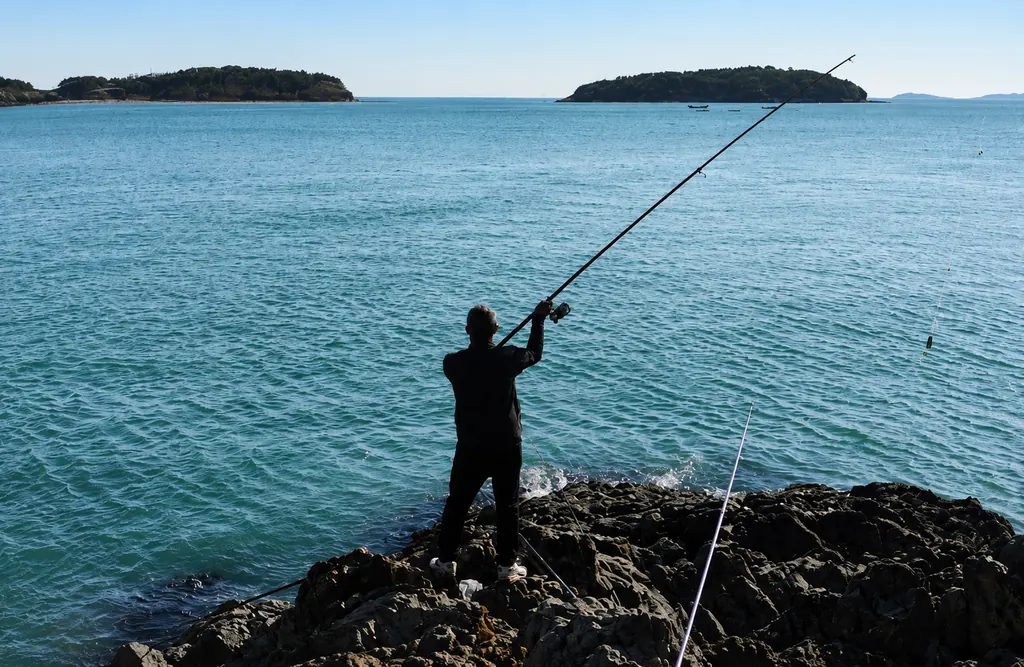 An angler casting from the rocks at a river estuary